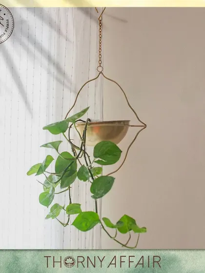 My hanging metal planters are designed to be a piece of art. This one features a unique, lip-shaped frame that cradles a small brass pot, perfect for trailing plants like pothos.