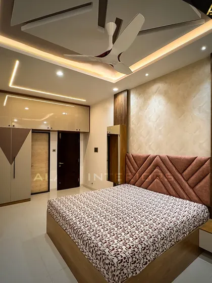 A contemporary bedroom with a geometric-patterned headboard and matching wardrobe doors. The false ceiling with cove lighting adds a touch of modern elegance.