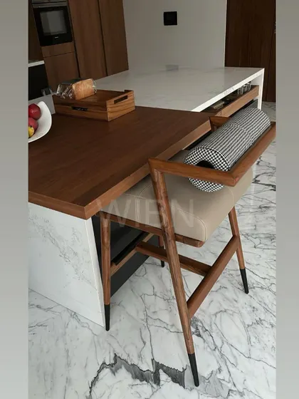 Our bespoke barstool, now nestled in its new home. This piece, with its solid wood frame, black-tipped legs, and upholstered seat and backrest, adds a touch of functional elegance to the client's kitchen island.