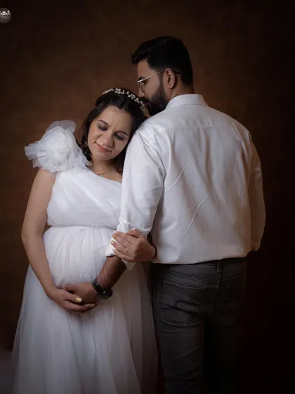 A gentle and supportive pose for a couple's maternity portrait. The contrast between his simple shirt and her ethereal white gown creates a beautiful visual balance.