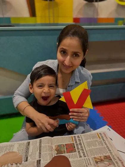 A toddler's joyful expression says it all. He and his mother hold up their letter 'V' craft, celebrating their creative work together.