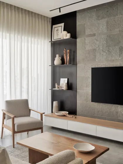 The TV wall in this living room is both a focal point and a functional feature. Adorned with contemporary metal shelves and a floating console of oak and matte white PU, it provides personalized display space against a serene grey limestone backdrop.