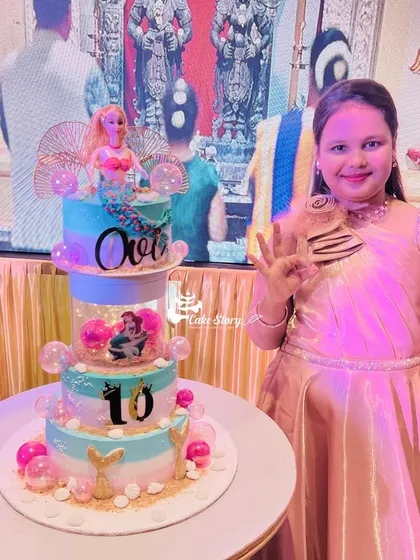 The birthday girl posing proudly with her amazing three-tier mermaid cake. It's always a joy to see such happy faces!
