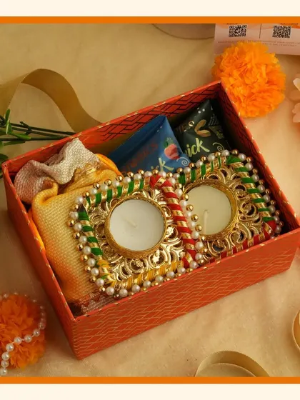 A small orange gift box containing two decorative diyas and a potli bag, a perfect small-scale Diwali gift or add-on.