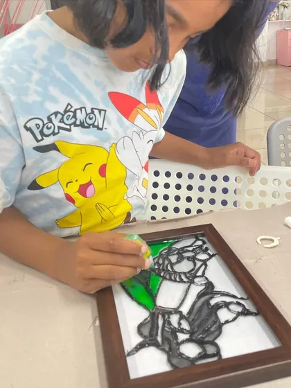 A young artist works on a glass painting, learning how to use special paints to create a stained-glass effect.