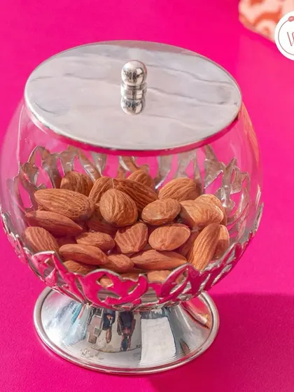 A beautiful silver and glass jar filled with almonds. This is a classic and elegant way to gift dry fruits as a wedding favor.