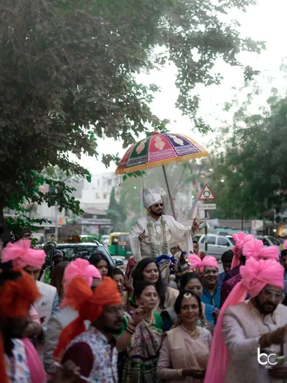 The groom's procession through the streets, surrounded by his family and friends in vibrant pink turbans, creating a festive atmosphere.