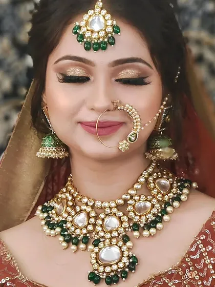 A close-up of a bride wearing a Kundan set with large, heart-shaped stones and green bead drops. A lovely and romantic choice.