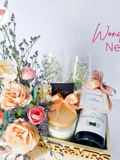 The 'Wonder Nest' hamper is a perfect gift for a new couple. It includes a bottle of non-alcoholic wine, elegant glasses, a scented candle, and gourmet chocolates, all nestled in a personalized 'Mr & Mrs' wooden tray.