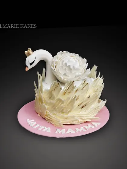 An elegant swan cake. The design features a graceful fondant swan, a large sugar peony, and delicate white chocolate shards to represent feathers.