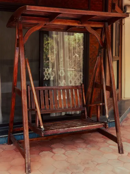 A classic wooden swing on a tiled porch, inviting you to sit back and enjoy a slow, peaceful moment.