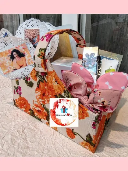 A unique, custom-made fabric basket with a vibrant orange floral print. This reusable basket is filled with personalized items, including photos, showing a creative and sustainable approach to gift packaging.