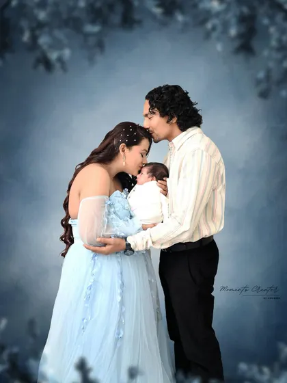 A dreamy and romantic newborn portrait. The parents tenderly kiss their baby's head, surrounded by a soft, ethereal blue background that makes the moment feel magical.