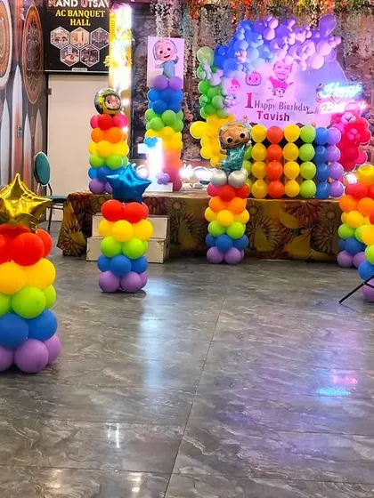 A full view of a Cocomelon themed party in a banquet hall, showing the stage and the arrangement of colorful balloon pillars in the foreground.