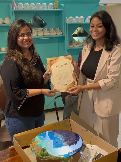 A participant receiving her certificate for completing the resin art workshop, with her beautiful ocean themed art piece.