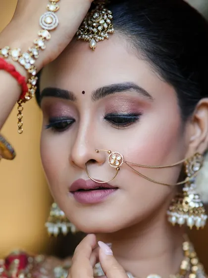A beautiful and traditional bridal pose. The makeup is classic and elegant, with a focus on the eyes and the intricate details of the nath and other jewelry.