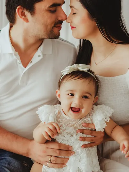A candid and joyful family portrait. The baby's bright smile is the center of this loving moment between her and her parents.