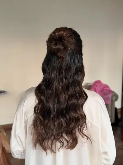 A chic and modern half-up, half-down hairstyle with a top knot and beachy waves. This look is perfect for a pre-wedding event or a casual brunch.