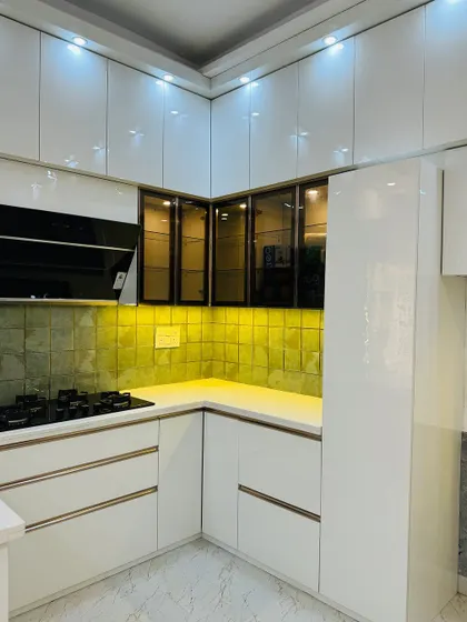 Another view of the all-white modular kitchen, showing the corner cabinet solution and the elegant glass-fronted upper cabinets.
