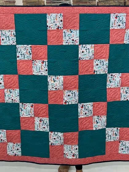 This four-patch quilt combines solid colors with a playful dinosaur and giraffe print fabric, making it a fun and modern choice for a child's room.