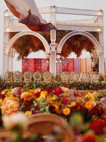 A view of the sunset mandap from the guest's perspective, with a foreground of lush, warm-toned florals creating a rich, layered look.