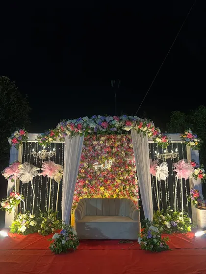 A wider shot of the stunning floral Nikah stage at night. The combination of the flower wall, neon sign, and chandeliers creates a truly magical setting.