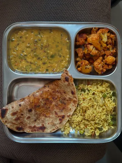 This plate features a stuffed paratha with dal methi, cauliflower palya, and a portion of vegetable rice, offering a variety of flavors and textures.