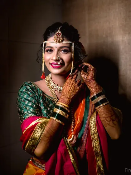 A close-up bridal portrait showing the bride adjusting her earring, drawing attention to her detailed jewelry and happy expression.