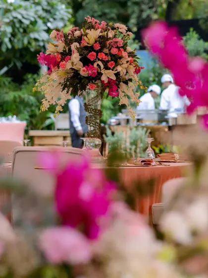 A beautifully composed shot through the flowers, capturing the ambiance of the elegant outdoor event with the catering station visible in the background.