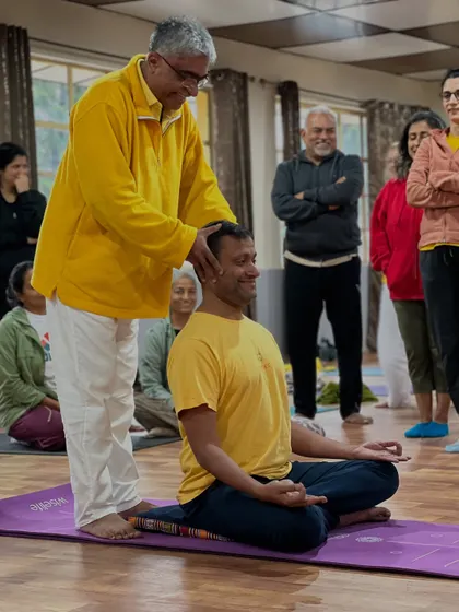 A teacher makes a gentle adjustment to a student's head alignment during meditation practice. This ensures the neck and spine are straight, promoting alertness and focus.