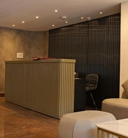 The reception desk for the hotel, featuring a fluted texture and a minimalist design. Behind it, a dark, vertically slatted wall adds depth and a contrasting texture, creating a sophisticated and modern check-in experience.