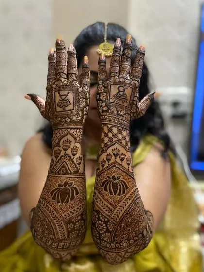 A bride showing off her full-arm mehandi, which features large lotus motifs and traditional symbols like the kalash.