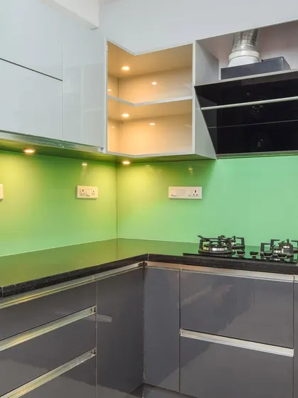 A close-up of the cooking area, featuring a modern chimney and hob. The glossy finish on the cabinets and backsplash is not only stylish but also easy to clean and maintain.
