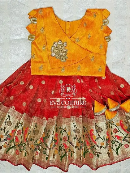 A beautiful pattu lehenga for a 6-month-old. The yellow blouse has a modern wrap-style design, and the red skirt features a woven Paithani-style border with bird motifs.