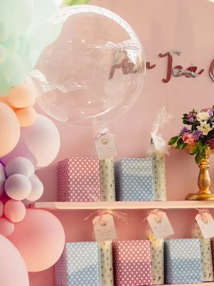 A close-up of the gift and favor display for a pastel-themed party. The setup includes a balloon garland and neatly arranged gift boxes on a shelf.