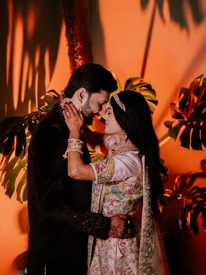 An intimate portrait of the couple against a warm, orange-lit backdrop with tropical leaves.