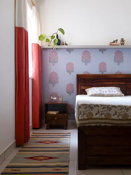 The guest bedroom, featuring a whimsical floral wallpaper and two-tone curtains. A ledge above the wallpaper offers a spot to showcase miniature brass decor pieces.