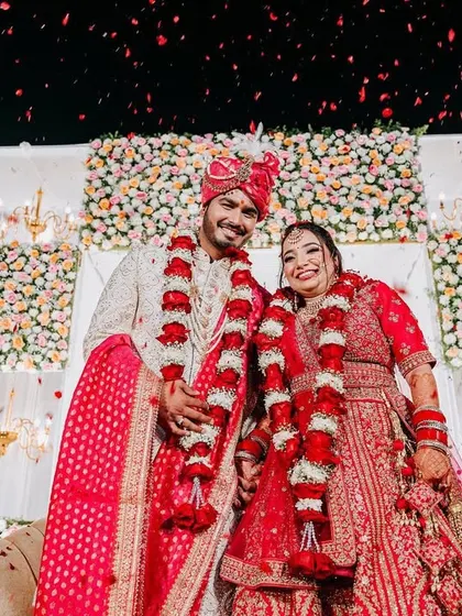 The couple stands for their Varmala ceremony, framed by a stunning backdrop of alternating floral panels and chandeliers.