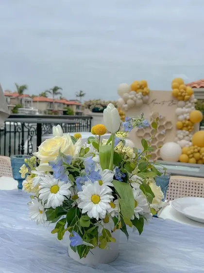 An outdoor "Mom to Bee" celebration, with the decor set up on a beautiful terrace. The tablescape with fresh daisies complements the yellow and white theme of the main backdrop.