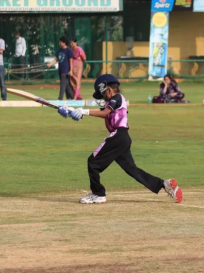 A young girl plays a confident drive shot during a U-10 match, with parents watching in the background.