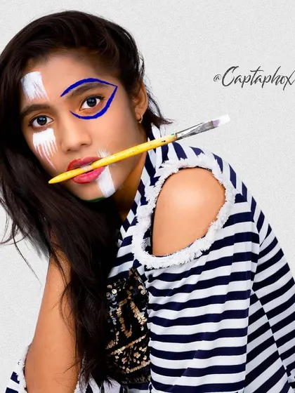 A creative fashion portrait where face paint becomes part of the look. The pose and striped outfit complement the artistic makeup, resulting in a modern and stylish editorial photograph.
