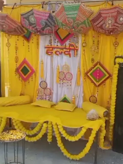 A cozy Haldi seating area on a 'charpai' (traditional cot) decorated with yellow fabric and colorful props like umbrellas and kites.