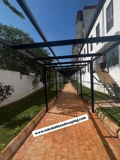 A view from inside the metal pergola at the Partha construction site, looking down the long, paved walkway bordered by a new lawn.