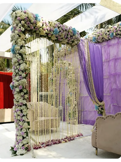 An intimate Nikah seating area, beautifully decorated with lavender drapes and an arch of white and blue flowers. The strings of jasmine flowers add a traditional and fragrant element.