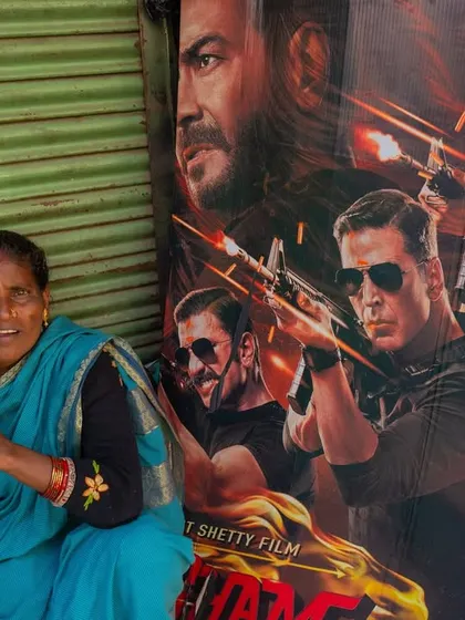 A woman sits on the street next to a large Bollywood movie poster in Kolkata. This image captures the interesting contrast between everyday life and the world of cinema.