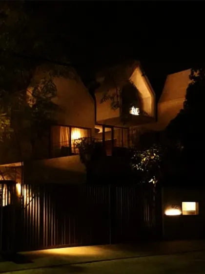 The Pyramids residence seen at night. The building's unique form, with its sloping roofs and articulated volumes, is highlighted by carefully placed exterior lighting.