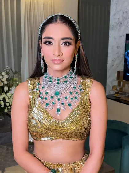 The bride looking radiant in her golden Manish Malhotra outfit, her hair styled elegantly with a statement headband and soft curls.