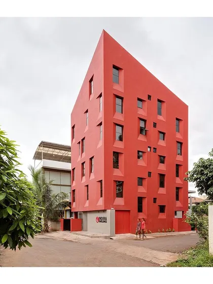The building's monolithic red form makes a strong statement in its residential context, while the carefully placed windows maintain privacy for the inhabitants.