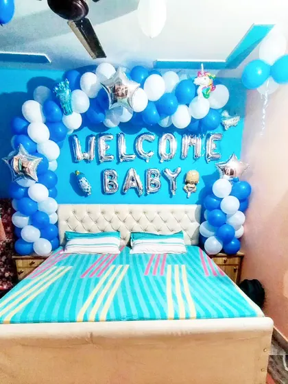A full view of a 'Welcome Baby' boy decoration, with a blue and white balloon arch framing the headboard of the bed.