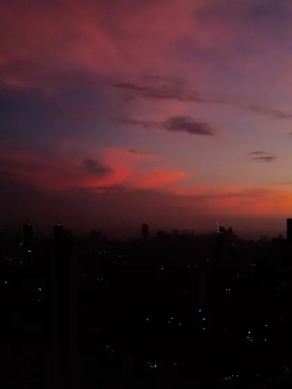 The silhouette of the Mumbai skyline is set against a dark, moody sky with streaks of orange and purple clouds after sunset.